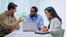 An adviser works with two clients at a conference room table in his office.