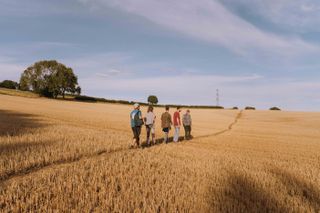 5 people walking through a field on a summers day