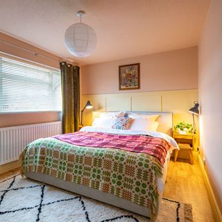 Bedroom with double bed and colourful blankets, bedside tables and lamps, green curtains