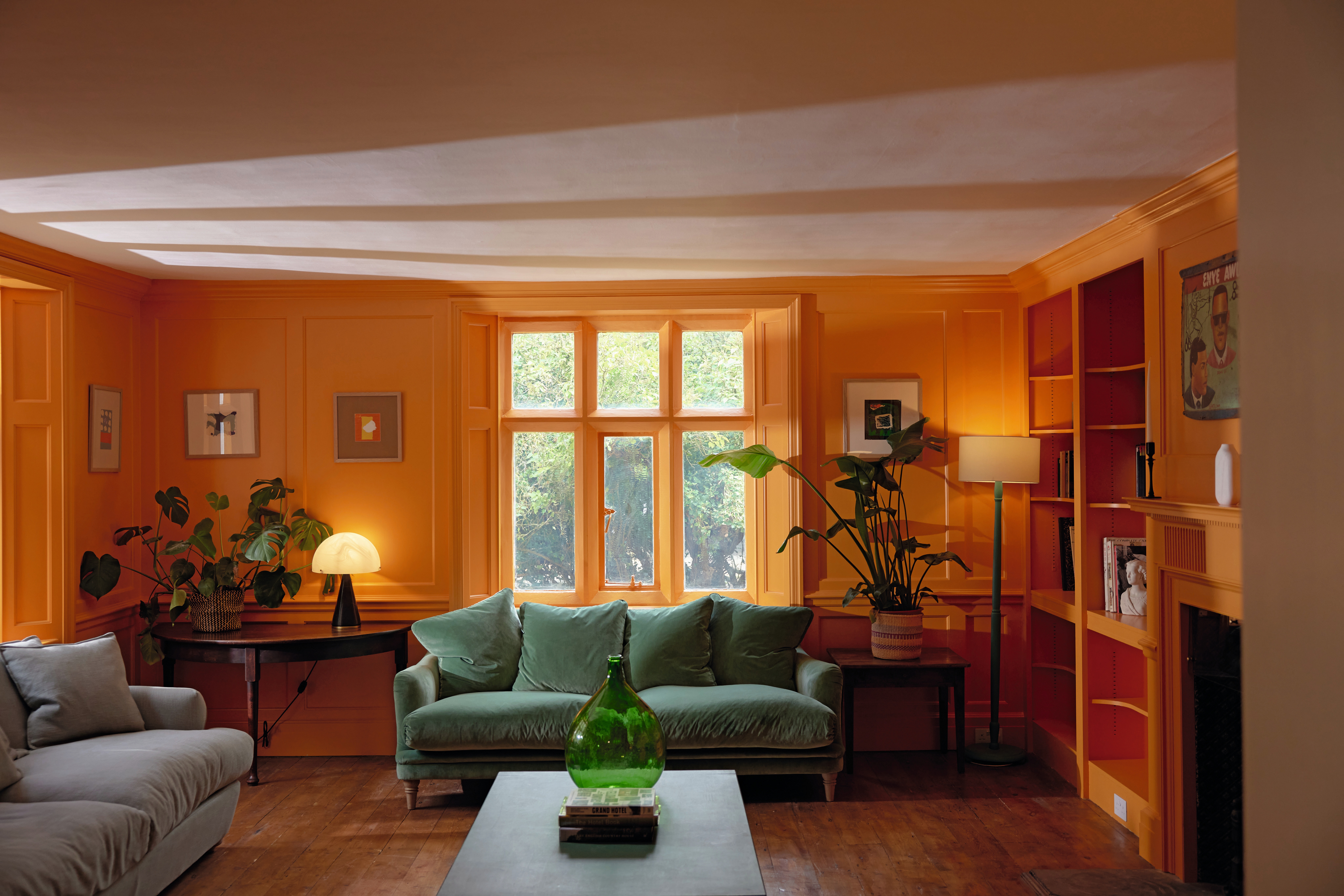 An orange-tinted, cozy living room decorated with a mushroom-shaped table lamp, framed artworks, plants, and plush couches.