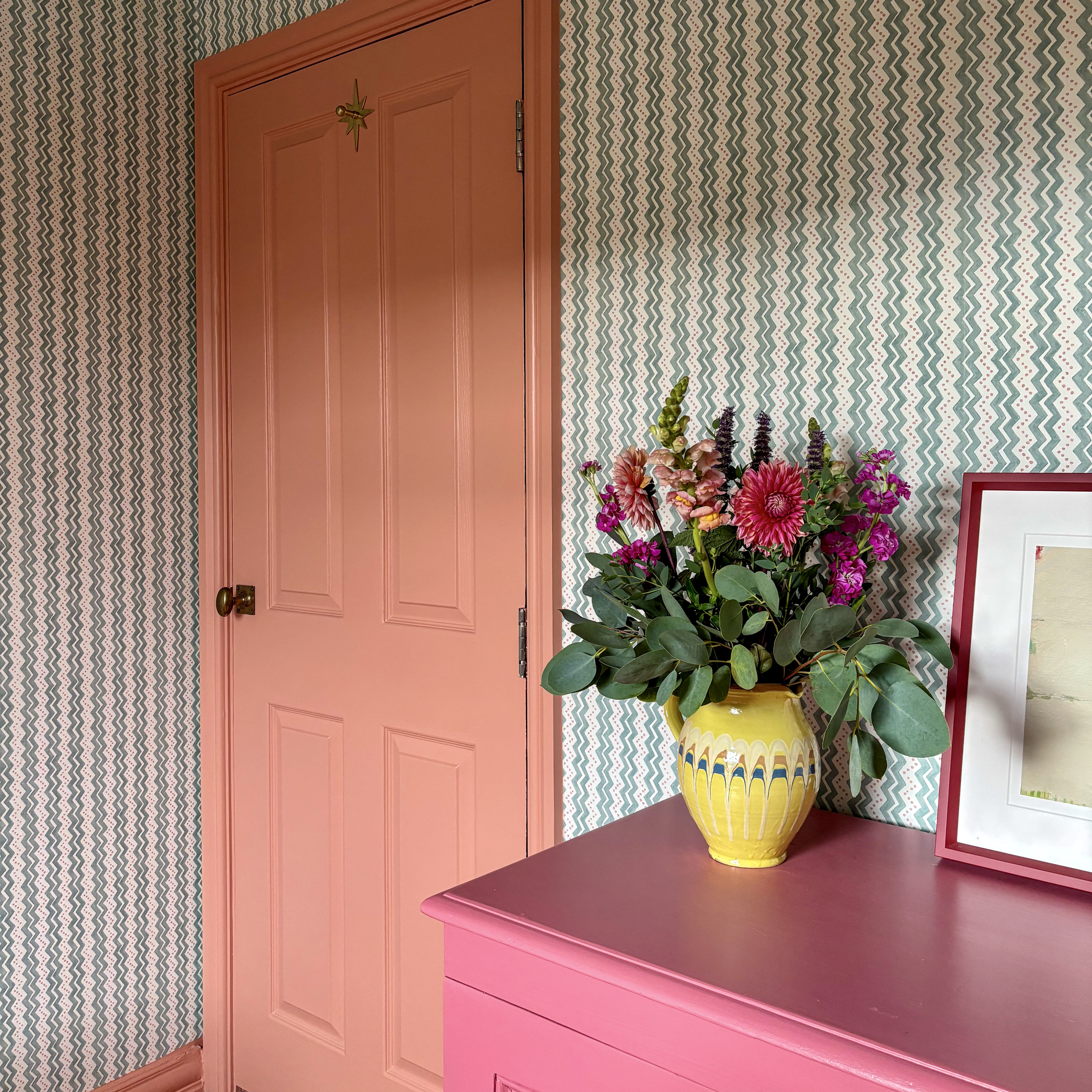 striped wallpaper on walls around a pink door and pink cabinet