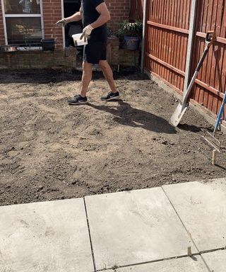 An image of a man using a garden roller to pack soil together and get rid of any air pockets in backyard