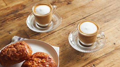 Two cups of coffee with pastries on a wooden dining table