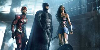 The Flash (Ezra Miller), Batman (Ben Affleck), and Wonder Woman (Gal Gadot) stand in a dark warehous