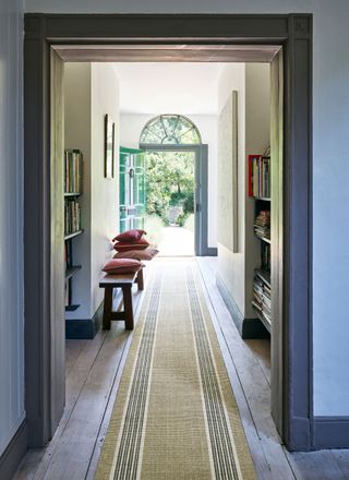 Long hallway looking towards an open door, with gray walls and a mustard striped runner.