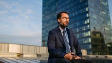 A businessman sits outside, a skyscraper in the background.