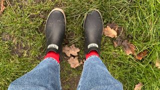 A person wearing Barbour Mallow welly boots with jeans and red socks on the grass