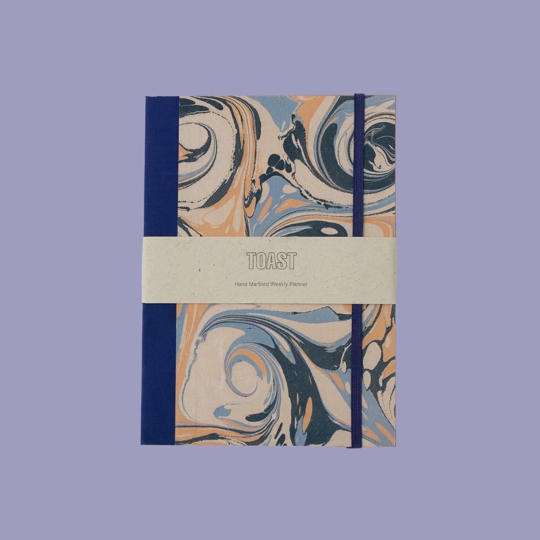 TOAST Hand Marbled Weekly Planner against pale purple background.