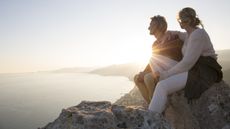 A couple take time to enjoy the sunset over the water while on a mountain hike.
