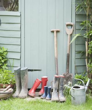 garden tools and wellies outside a green painted shed