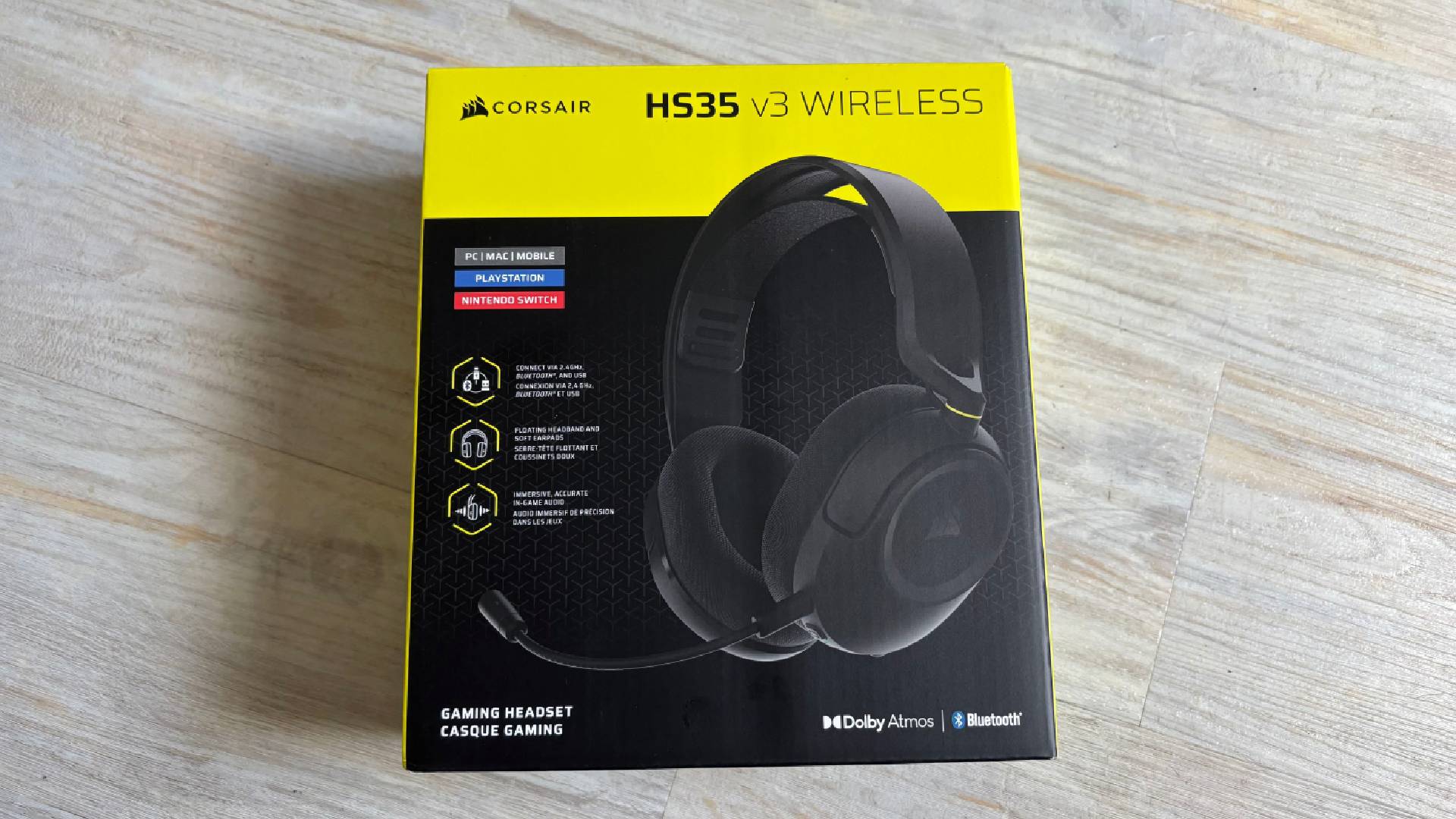 Corsair HS35 v3 box, showing yellow and black branding and details about the headset, against a white hardwood floor