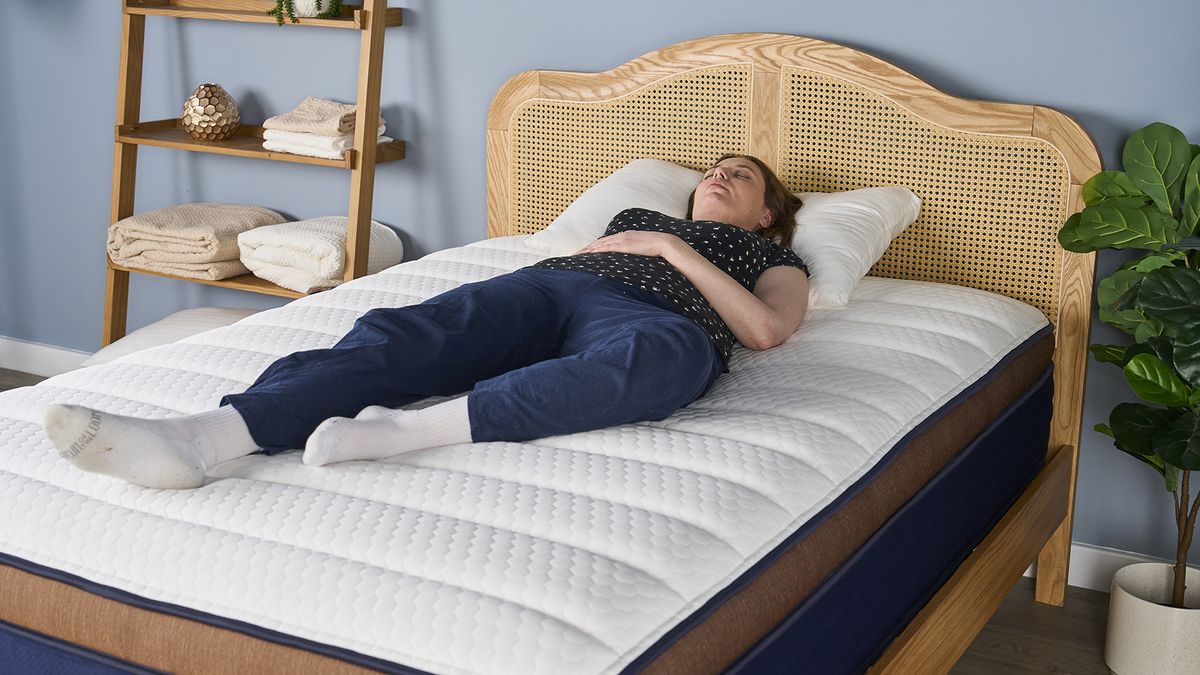 A girl wearing black and white pyjamas laying on her back on Brooklyn Bedding CopperFlex Pro Hybrid mattress with white surface and rattan bedframe