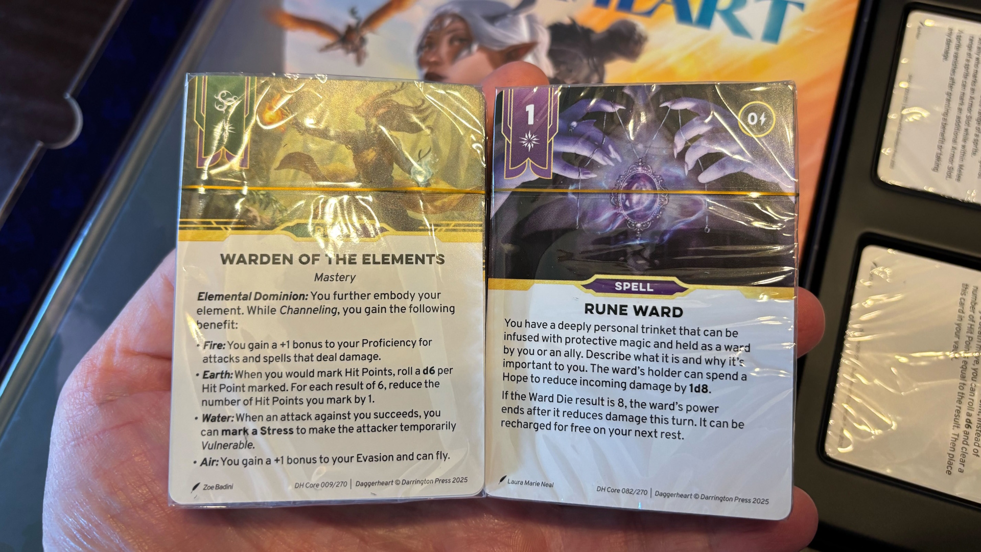 Photo of Daggerheart cards held in hand with Core Rulebook in background