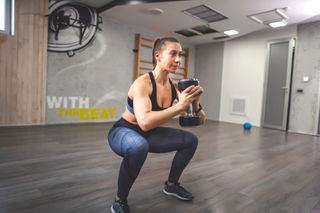 Female cyclist squatting with a dumbbell