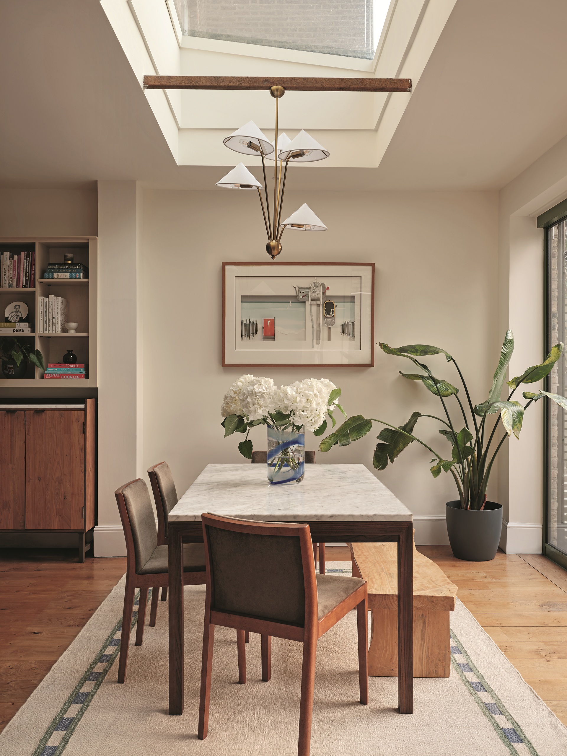 a white dining room with a dining table, under a skylight with pendant lighting underneath