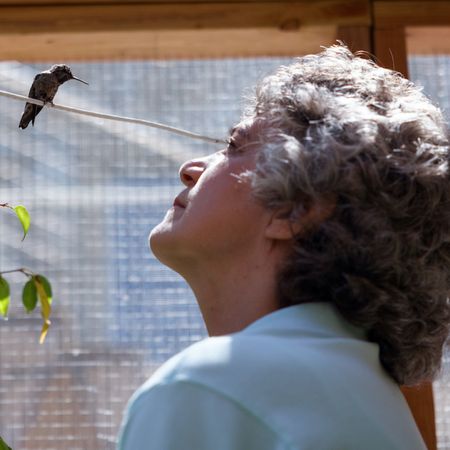 an older woman looks up at a hummingbird on a wire in a still from the documentary every little thing