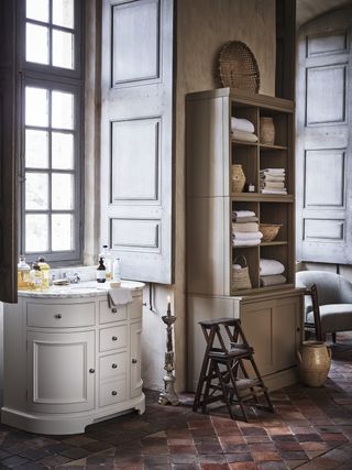 bathroom with white and marble curved vanity, freestanding shelving unit, vintage steps, armchair, terracotta floor tiles