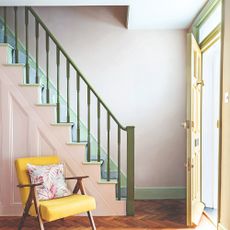 A hallway with a staircase with a pale pink base, olive green balustrade and mint green skirting boards
