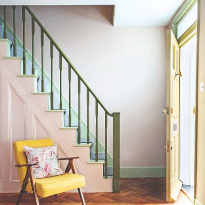 A hallway with a staircase with a pale pink base, olive green balustrade and mint green skirting boards