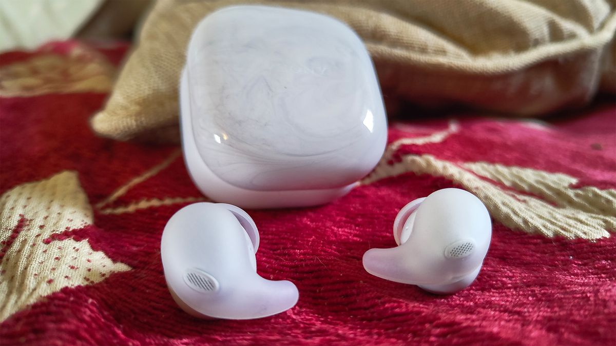 Sony LinkBuds Fit in-ear headphones in white, laying on a red fabric with the charging case in the background.