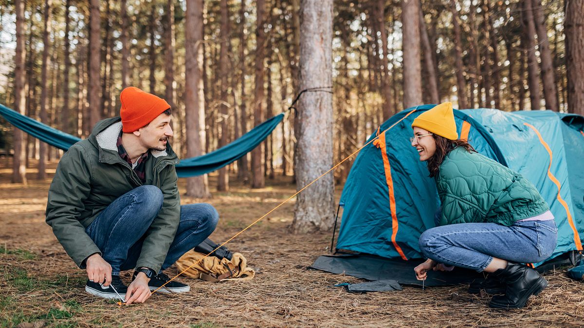 Cheerful and smiling campers set up a tent for camping in the woods.