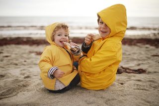 Brother and sister in yellow raincoats eating snacks while sitting on the beach