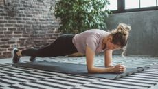 Woman doing plank exercise in home studio wearing activewear next to plant after finding out how long to hold a plank for