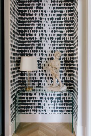 entryway with black and white wallpaper, glass console, lamp and sculpture