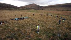 A wide angle shot of a circle of stones in the English moorland with people scattered around