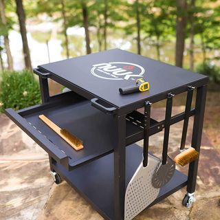 Black pizza oven stand with retractable shelf and utensils hanging on the side