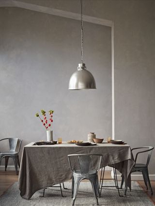 Gray dining space with gray walls, industrial style zinc chairs, factory pendant, and relaxed gray tablecloth draped informally.