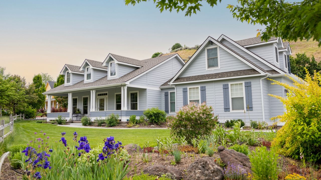 Exterior shot of large American home with large tidy lawn and small flowers and shrubs in foreground