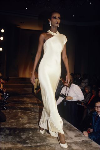 Mandatory Credit: Photo by Thomas Iannaccone/Penske Med/REX/Shutterstock (6905314d) Iman models a one-shoulder white dress with pearl necklace in the Bill Blass Spring 1986 RTW show Bill Blass Spring 1986 RTW, New York
