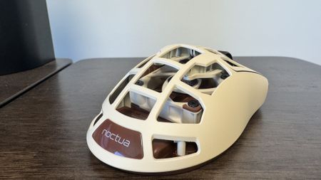 The Pulsar Feinmann F01 Noctua Edition gaming mouse on a wooden desk, from the back right showing off the Noctua logo