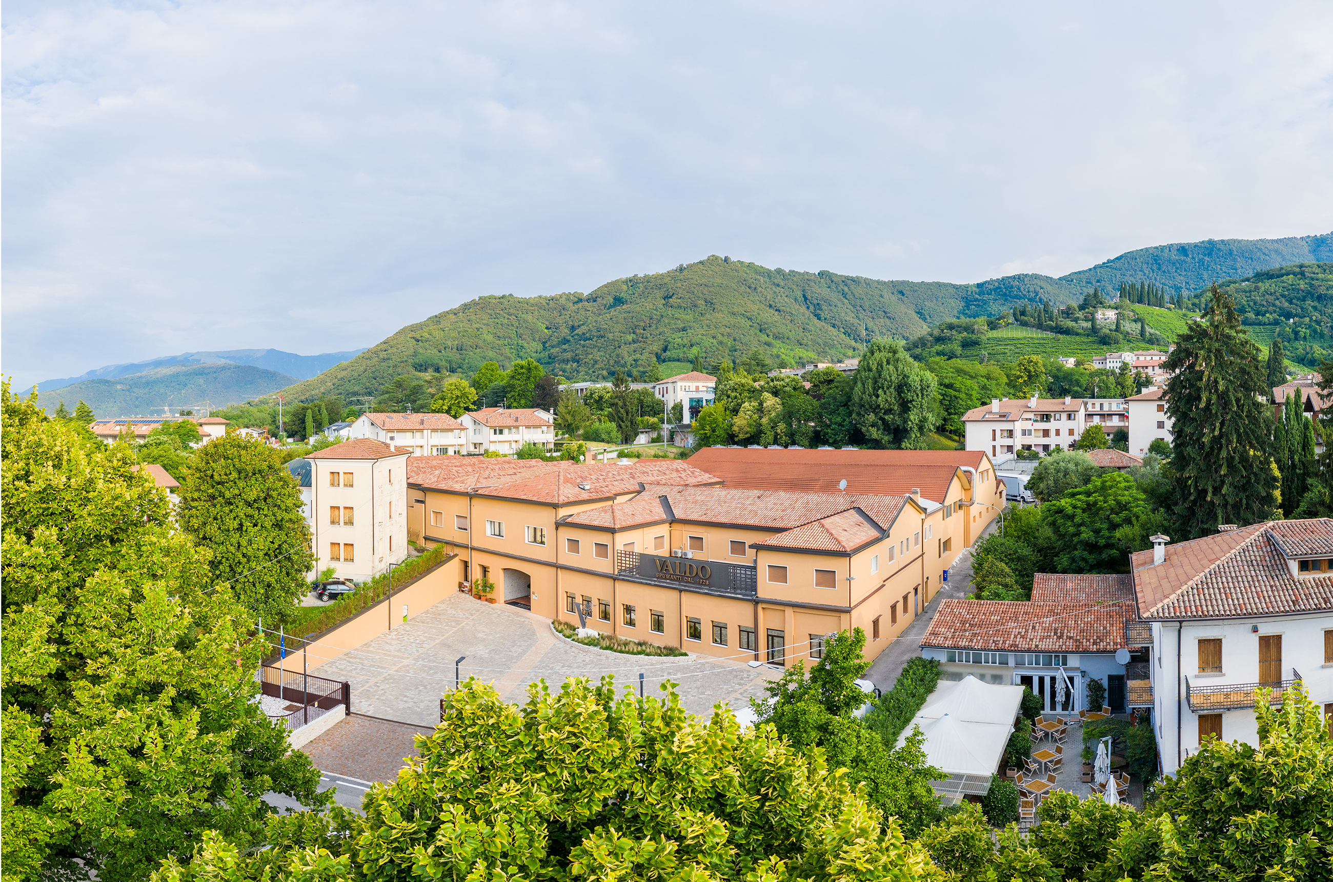 View of the Valdo winery (a peach coloured building) surrounded by green trees with hills in the background