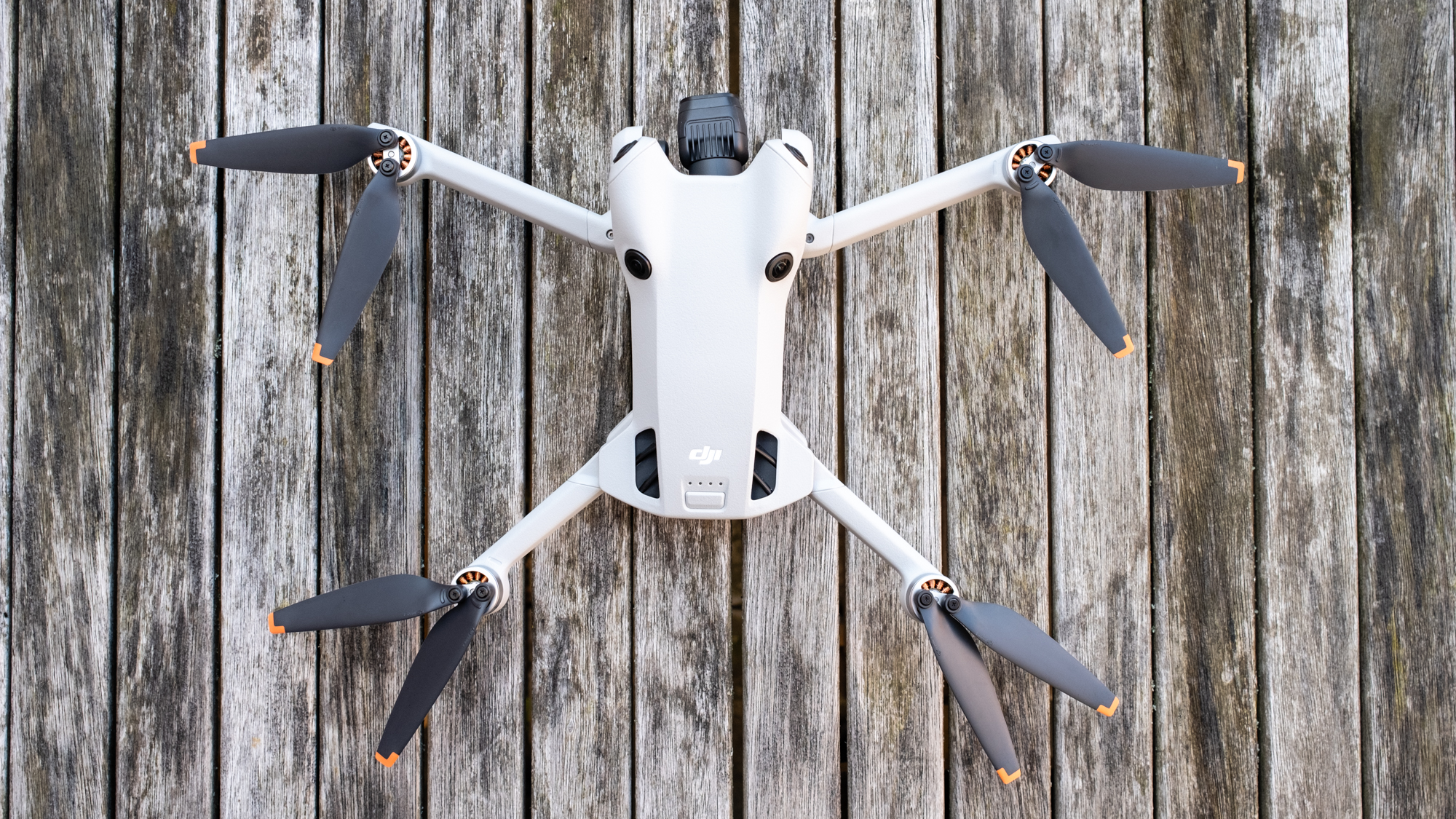 A top-down view of a white DJI Mini 4 Pro drone with its propellers out sitting on wooden slats.