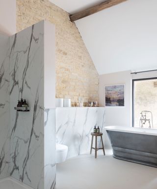 Neutral bathroom with exposed stone wall and freestanding tub in luxurious Cotswolds barn