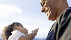 A young grandfather smiles, looking at his baby granddaughter.
