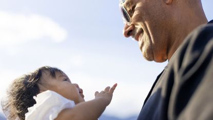 A young grandfather smiles, looking at his baby granddaughter.