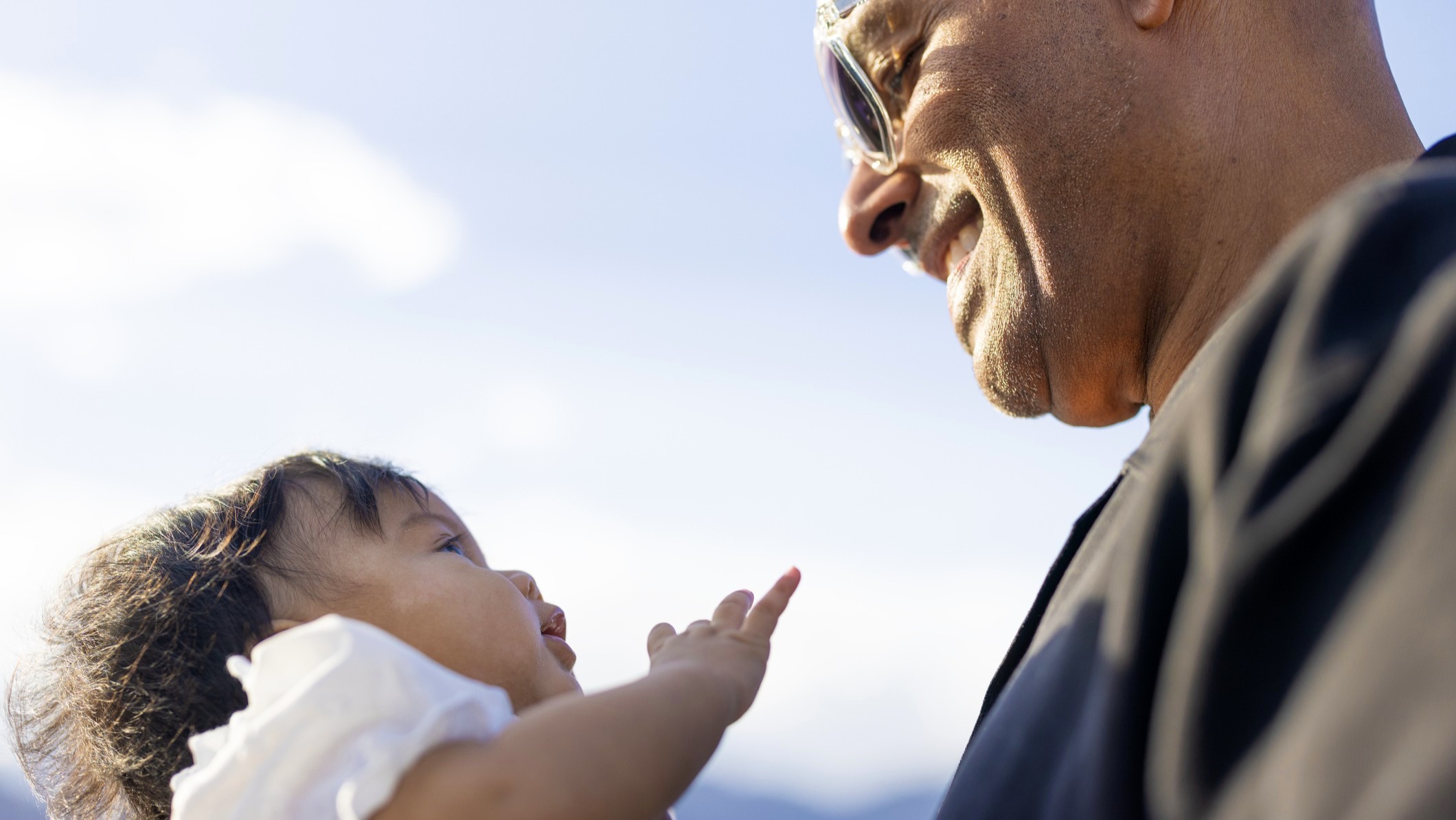 A young grandfather smiles, looking at his baby granddaughter.
