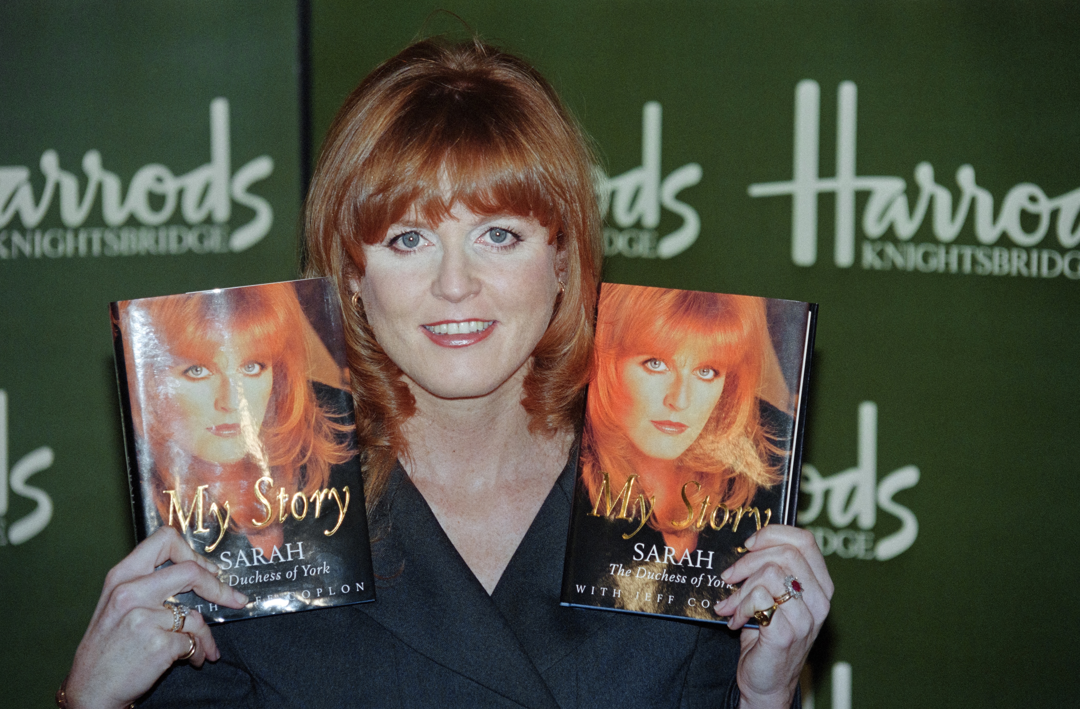 Sarah Ferguson holding up two copies of her memoir, My Story, in front of a Harrods background