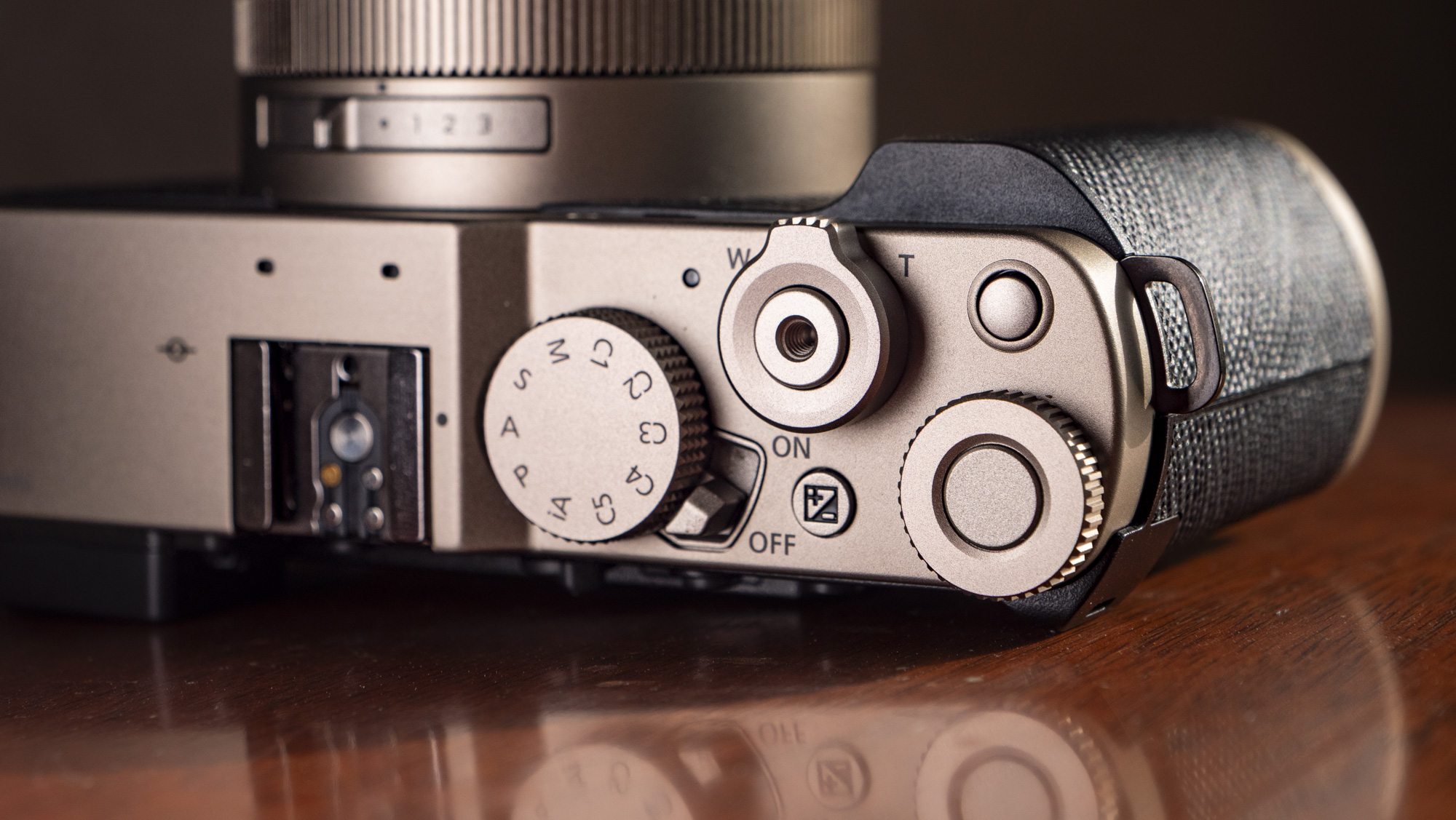 Closeup of the top plate of the Titanium Gold special edition of the Panasonic Lumix L10 compact camera, on an antique wooden table