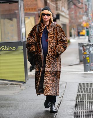 Jennifer Lawrence walks in New York City wearing a coat trend with black boots and a blue sweater