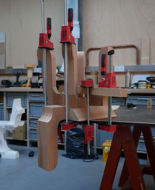 A wooden chair held together by red tenon joining tools in Max Lamb's studio