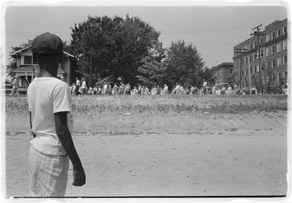 A boy watches a mob march by.