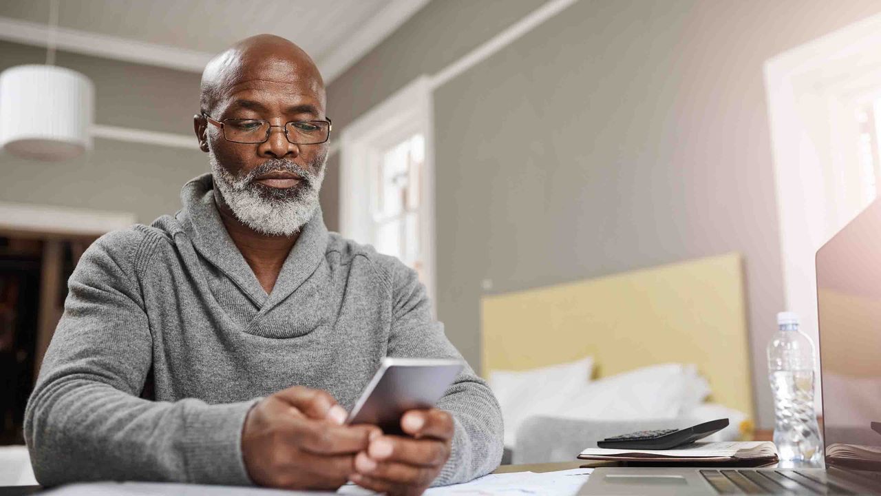 Photo of an older man looking at a computer screen and a calculator