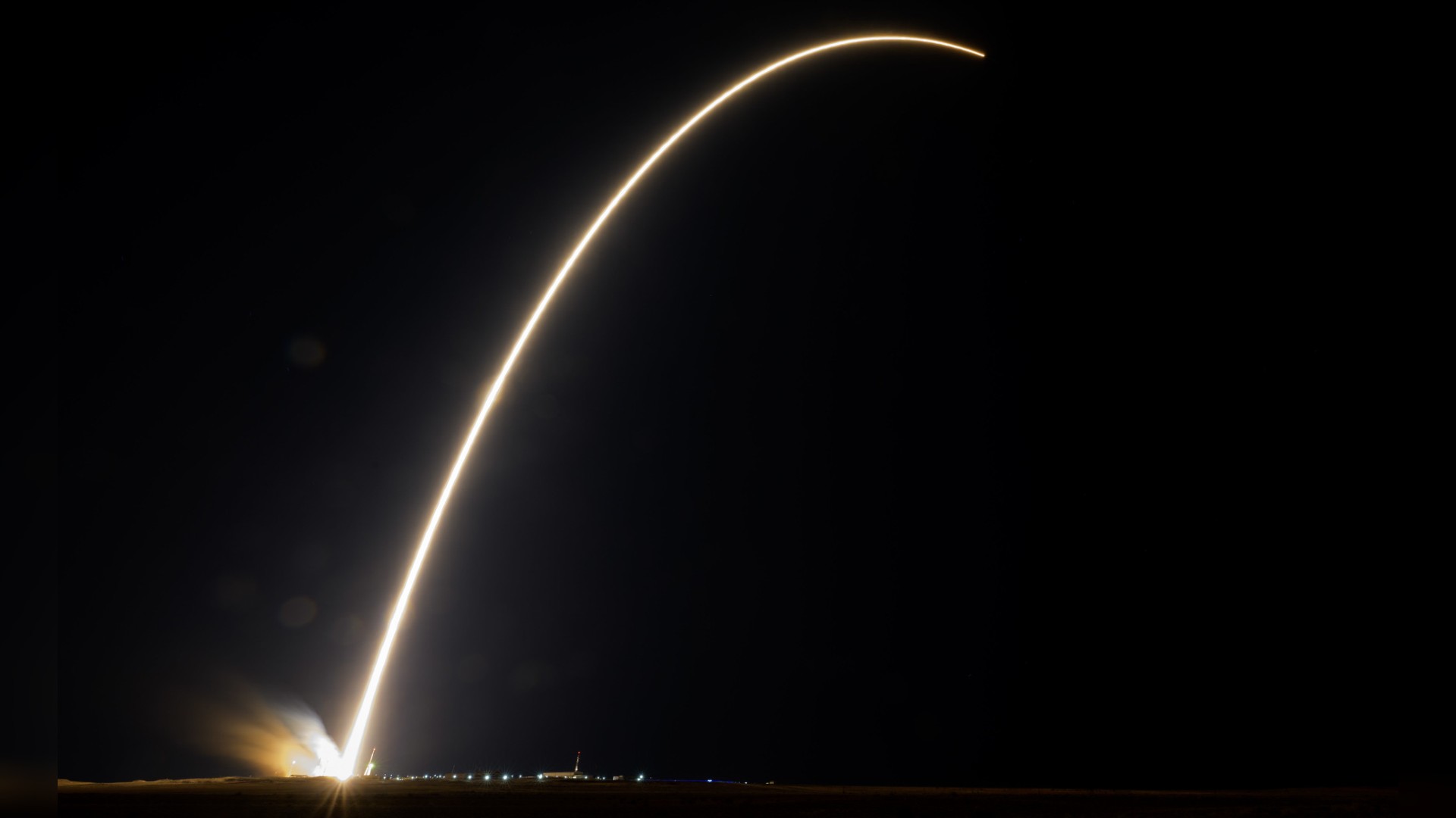 a rocket launches at night, leaving a streak of fire behind it