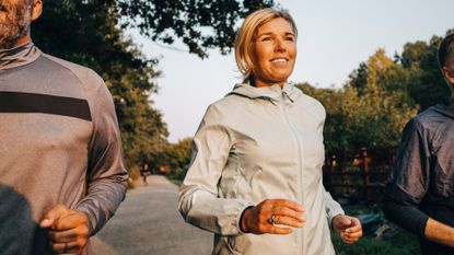 Woman jogging with two friends in summer light through a park on path wearing jacket with hair tied back, representing how many times a week should you run