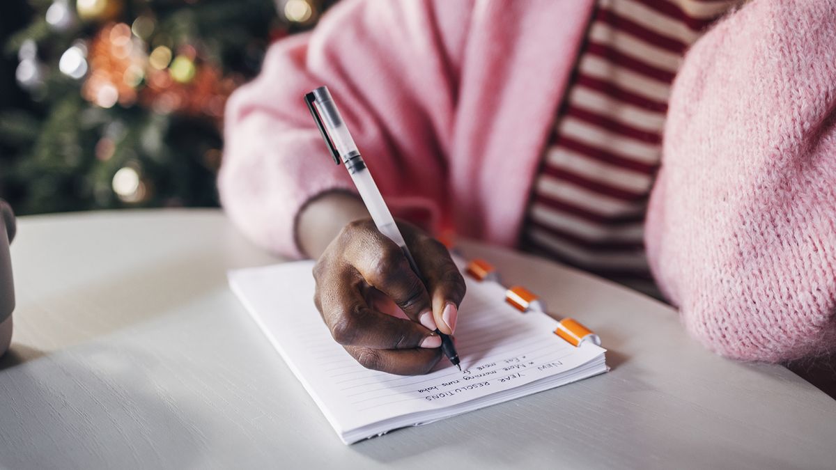 Woman writing her new years resolutions in a notebook on the table.