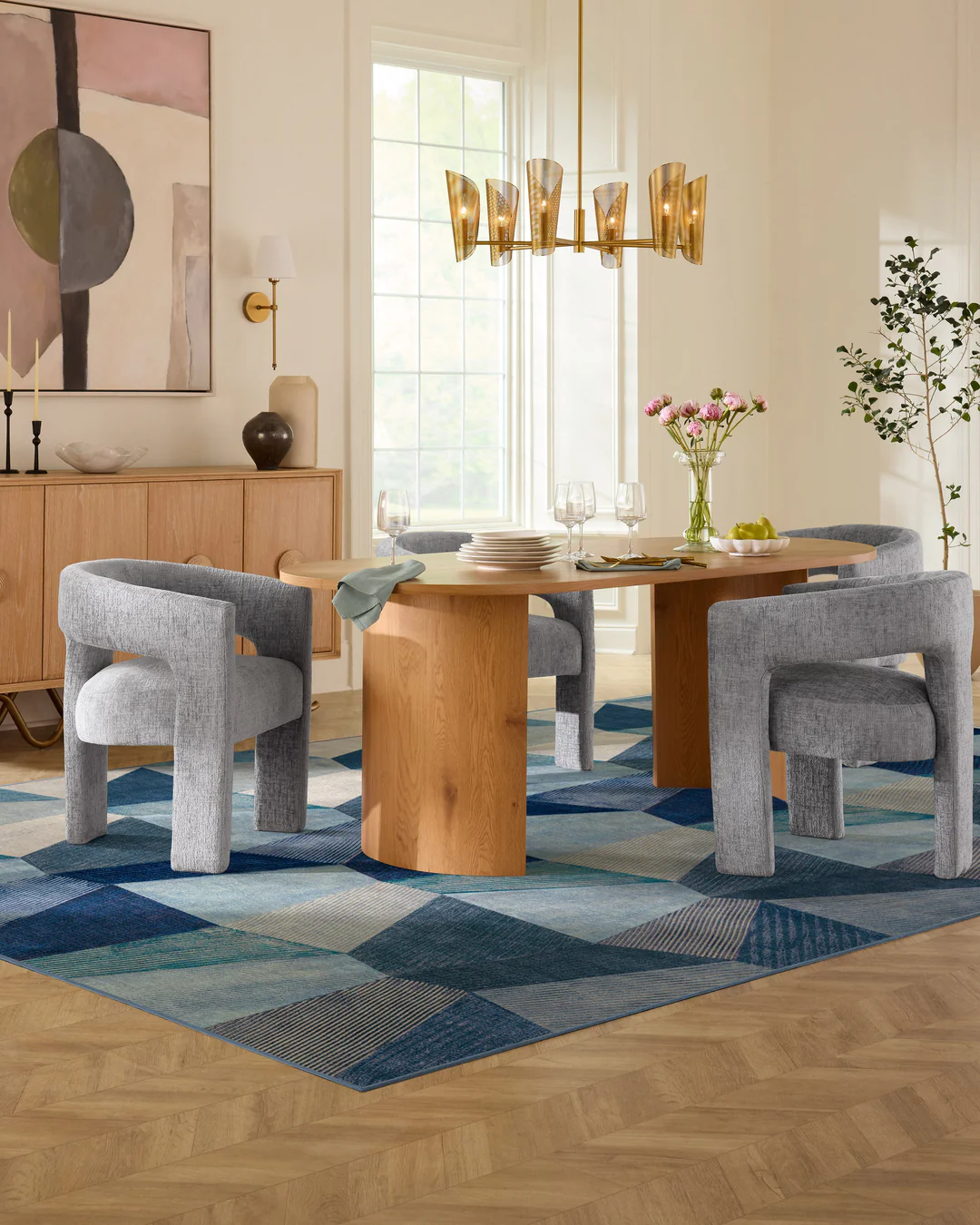 Bright dining room with a natural wood dining table surrounded by upholstered grey dining chairs, set on a blue geometric patchwork rug. Washable blue rug with pattern